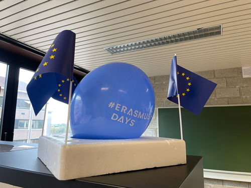 boulon bleu avec une inscription erasmus days en blanc dessus. Entouré de 2 drapeaux européen dans une classe de cours