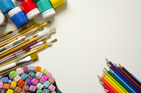 On a white background in the upper left corner there are paints (gouache), under them brushes of different sizes and a set of colored markers. In the lower right corner are colored pencils of twelve colors. Getting ready for art school. Children and creativity. Free space for entries.
