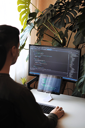 Young developer is working from home. Programmer coding using screen and tablet